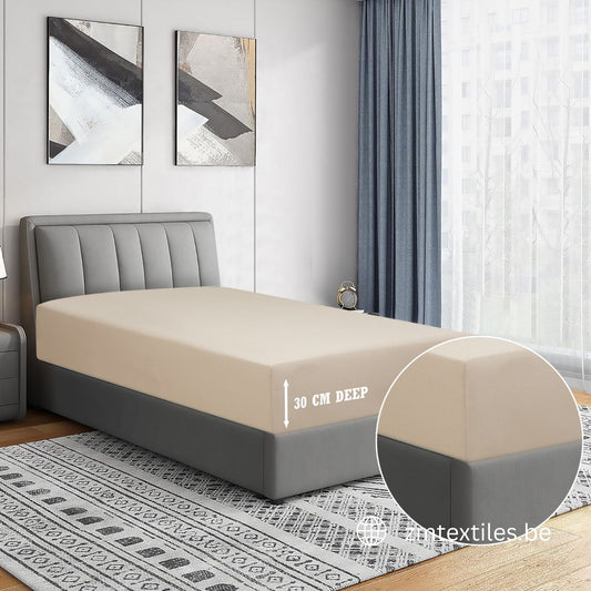 Beige fitted sheet on a bed with a gray headboard in a bedroom setting. featuring ZM Textiles T144 Cotton fitted sheets.