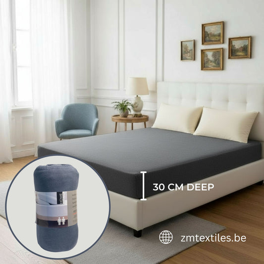 Gray mattress cover on a bed with an inset showing a rolled-up mattress cover and text indicating depth, set against a bedroom background, featuring ZM Textiles Belgium jersey fitted sheets.