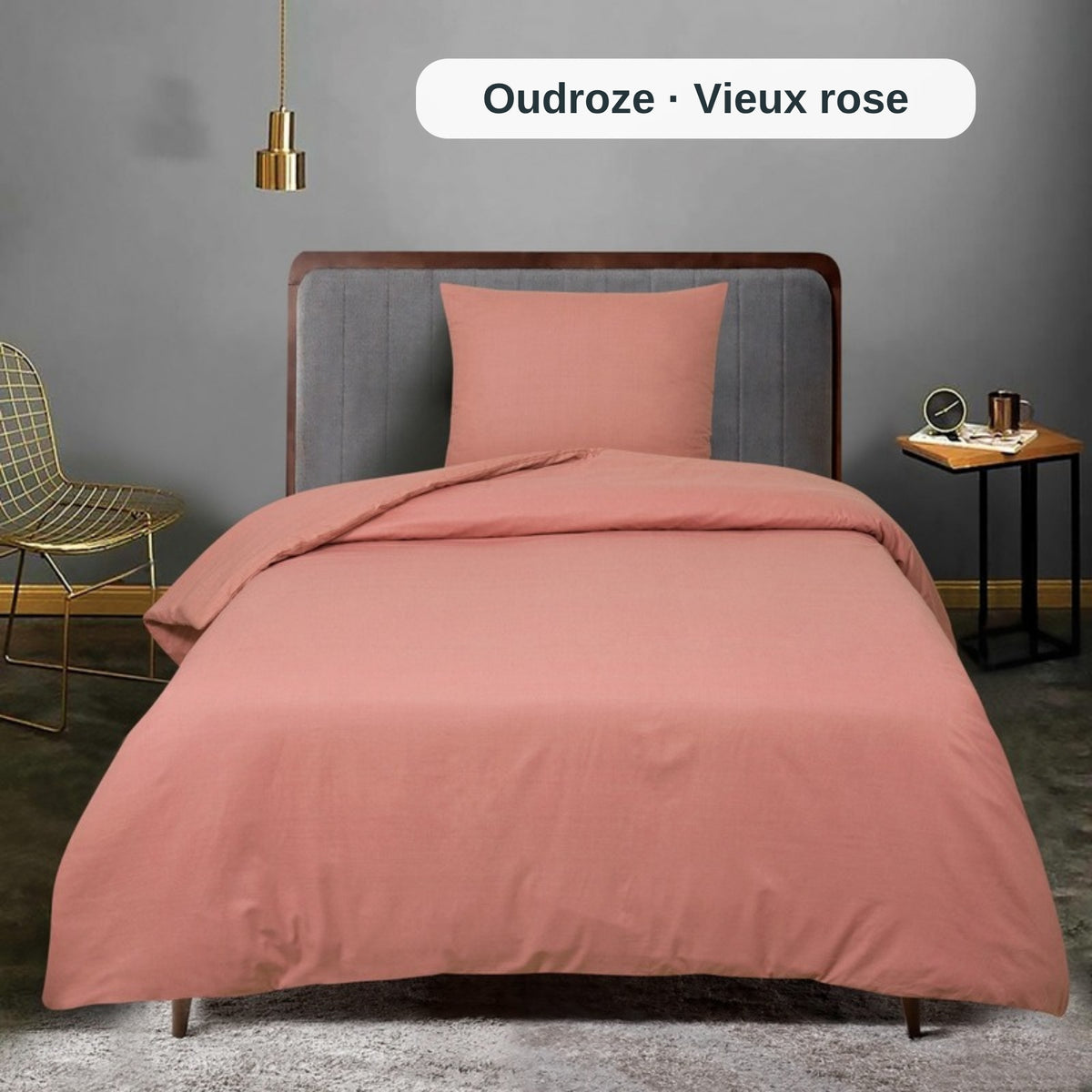 Bett mit rosa Bettwäsche in einem Raum mit grauer Wand und kleinem Tisch, mit dem uni Bettbezug-Set von ZM Textiles Belgium.