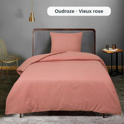 Bett mit rosa Bettwäsche in einem Raum mit grauer Wand und kleinem Tisch, mit dem uni Bettbezug-Set von ZM Textiles Belgium.