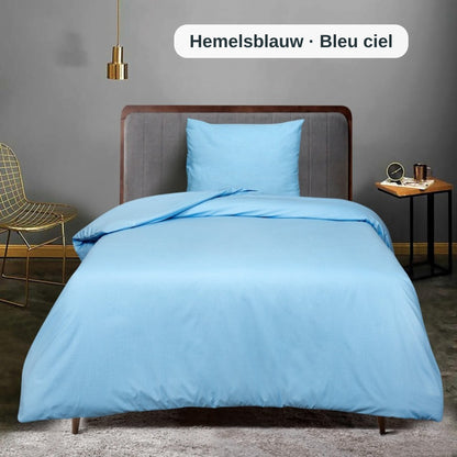 Blaues Bettwäsche-Set auf einem Bett in einem modernen Schlafzimmer mit grauer Wand und hölzernem Nachttisch, mit dem uni Bettbezug-Set von ZM Textiles Belgium.