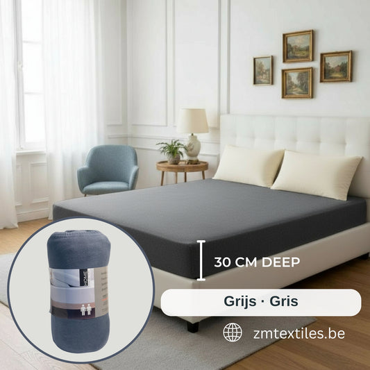 Protège-matelas gris sur un lit avec encart montrant un protège-matelas roulé et texte indiquant la hauteur, sur fond de chambre, présentant les draps-housses en jersey de ZM Textiles Belgium.